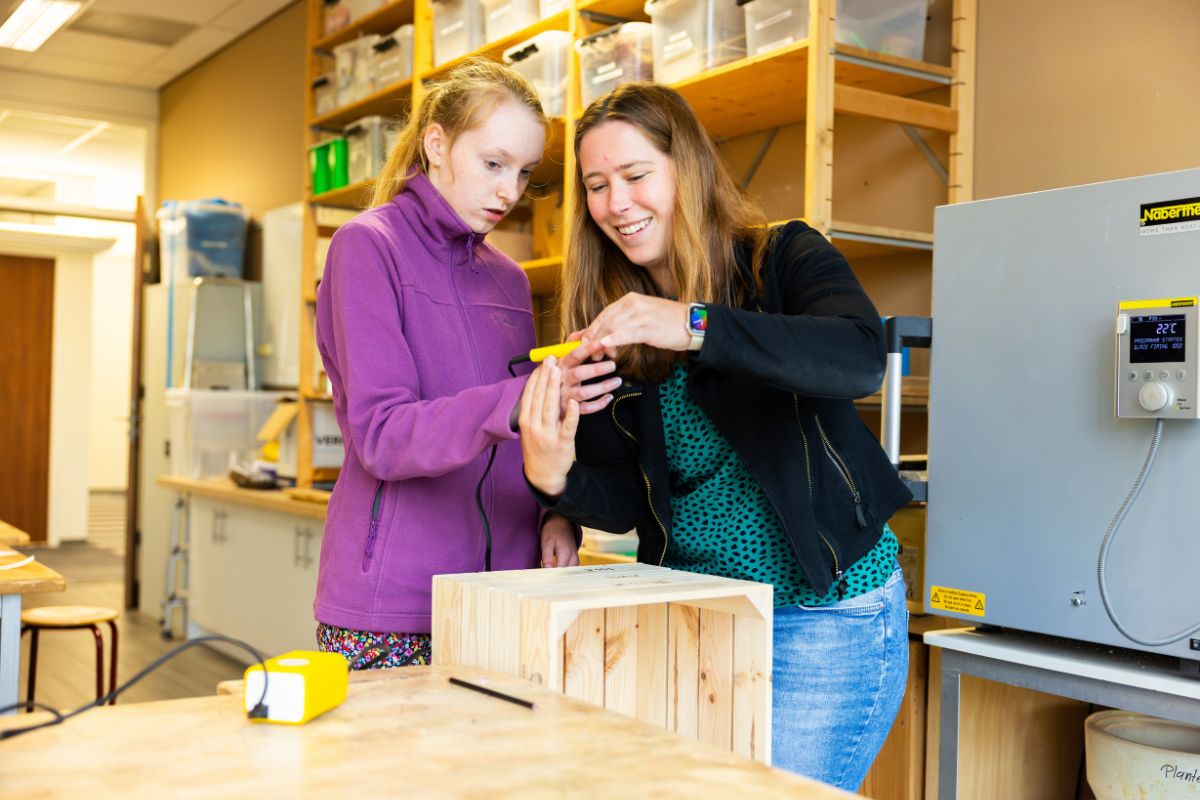 Begeleiding bij een praktijkopdracht Leerling krijgt uitleg van een docent tijdens het werken aan een houten project in het praktijklokaal.