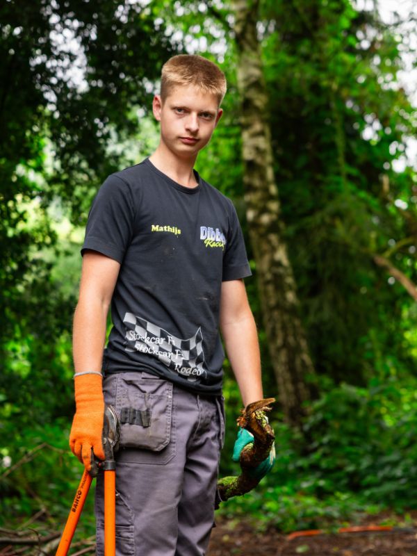 Buiten aan het werk in het groen Leerling werkt in een bosrijke omgeving met werkhandschoenen en gereedschap tijdens een praktijkmoment in het groen
