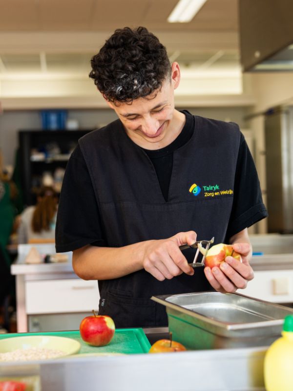 Fruit voorbereiden in de praktijkkeuken Leerling schilt een appel in de praktijkkeuken tijdens een kookles gericht op zelfstandigheid en werkvaardigheden