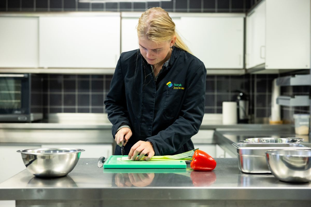Koken als praktijkervaring Leerling snijdt groenten in de praktijkkeuken tijdens een kookles gericht op werkvaardigheden