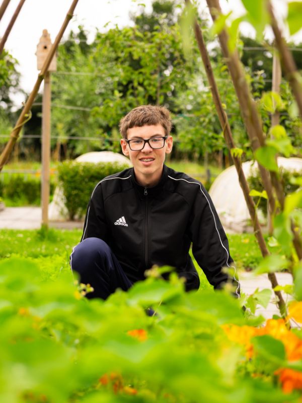 Leerling werkt in de schooltuin van Talryk Leerling zit tussen groene planten in de schooltuin en werkt aan tuinonderhoud in een rustige, natuurlijke omgeving