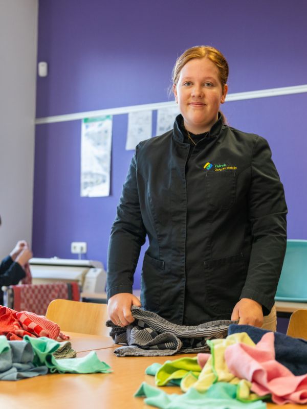 Oefenen met huishoudelijke taken Leerling staat in het klaslokaal en vouwt wasgoed tijdens een praktijkles gericht op zelfstandigheid en huishoudelijke vaardigheden