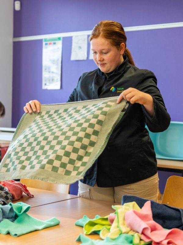 Praktijkles textiel Leerling vouwt een theedoek tijdens een praktijkles textielverzorging in het klaslokaal