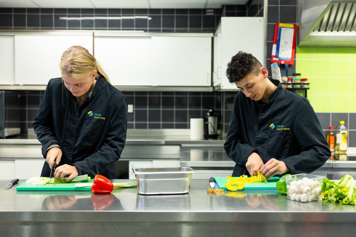 Samen koken in de praktijkkeuken Leerlingen bereiden samen groenten tijdens een kookles in de praktijkkeuken