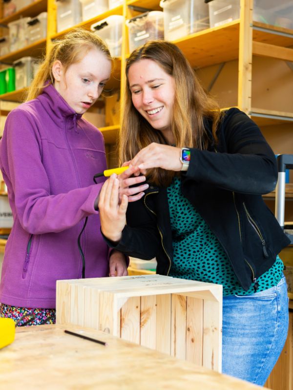 Samen werken aan een houtproject Leerling krijgt uitleg van een docent tijdens een praktijkles houtbewerking en werkt aan een houten project in het praktijklokaal
