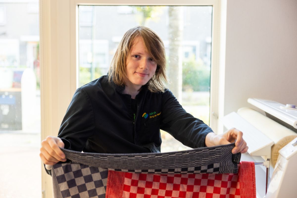 Zelfstandig werken in praktijk Leerling vouwt handdoeken bij een was- en strijkruimte tijdens een praktijkles gericht op huishoudelijke vaardigheden